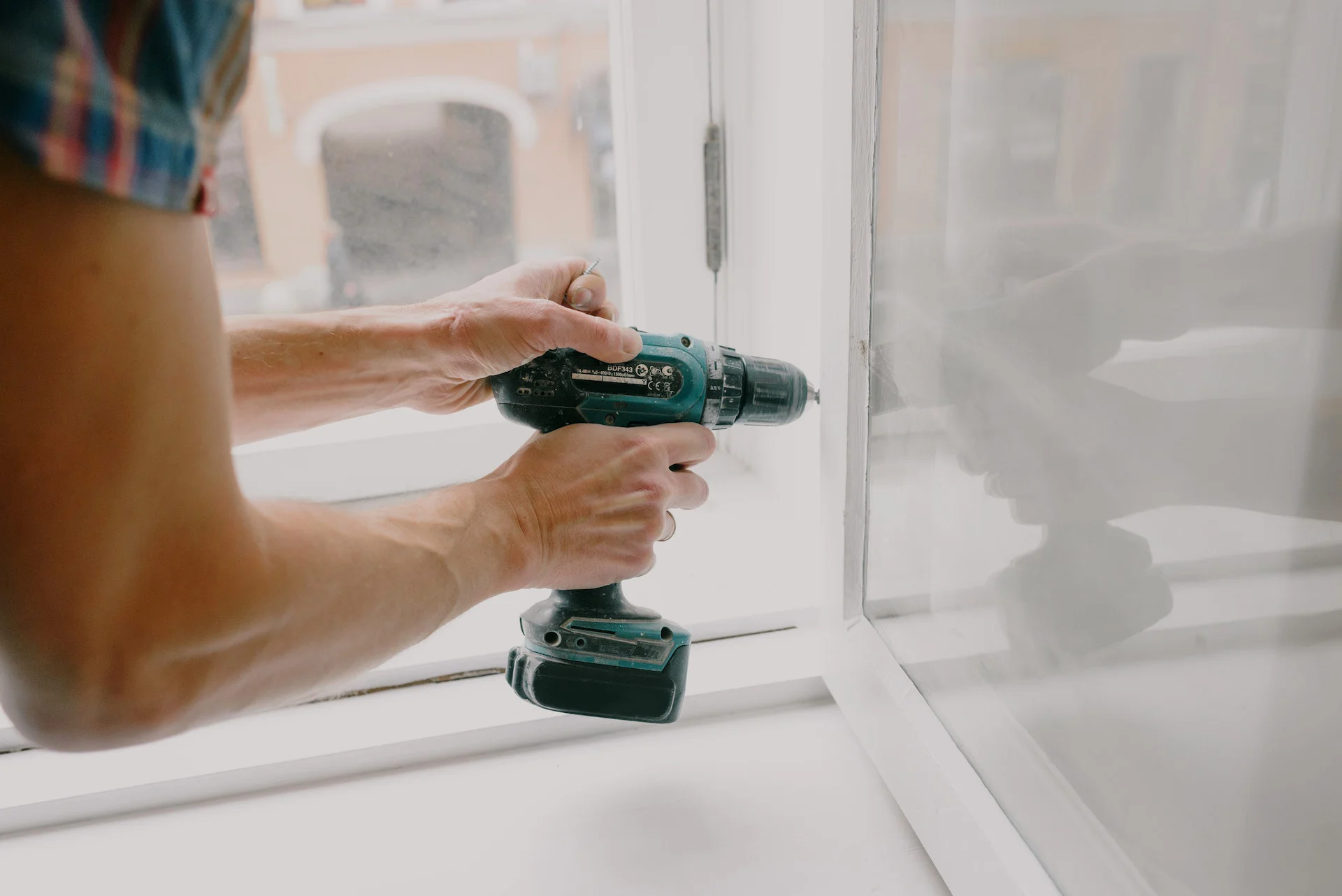 Drill fixing a white uPVC window frame
